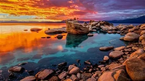 Dramatic sunset over rocky shoreline with turquoise water reflecting golden and purple sky